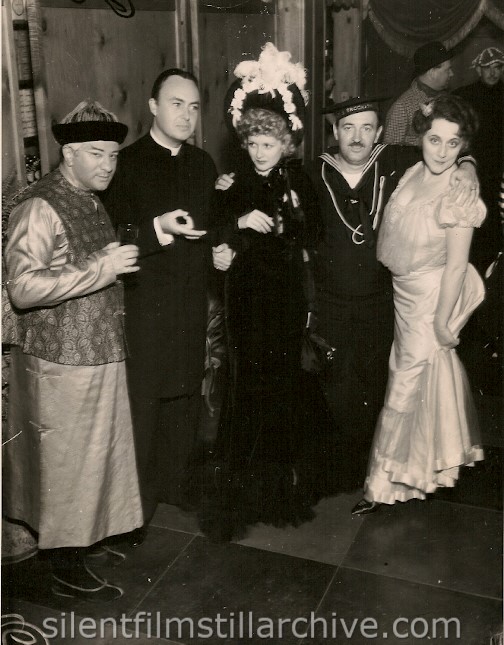 AT HOLLYWOOD BOWERY PARTY.
The Gay Nineties' influence has at last reached the party stage. At the "Old Bowery" party given in Hollywood by the Daryl Zanucks and William Goetzes, numerous film celebrities appeared in ancient and laugh-provooking costumes. Among them, were left to right: Harry Green, Gene Markey, Joan Bennett, Raymond Griffith and Mrs. Griffith (Bertha Mann)